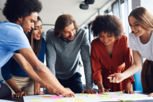 a group of employees crowds over a desk of papers to collaborate