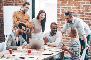 Group of cheerful young people discussing group health insurance plans with smiles and gesturing while leaning to the table in office