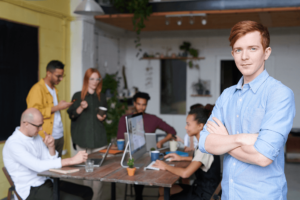 a male small business owner stands in the foreground of his employees