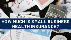 "How Much Is Small Business Health Insurance?" is written over a stack of papers, a calculator and a pair of eyeglasses on a desk.