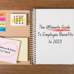 A notebook with "The Ultimate Guide To Employee Benefits In 2023" written on it is laid on a desk alongside post it notes and a pencil