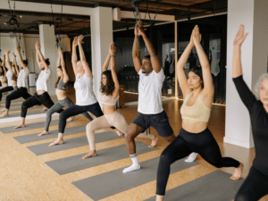 iverse group of people participating in a yoga class, lined up in warrior pose, highlighting workplace wellness and fitness initiatives.